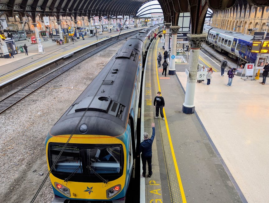 A modern train with a streamlined black and yellow front, situated on railway tracks at High Wycombe train station. The platform is busy with passengers, some walking and others waiting, amidst a cano