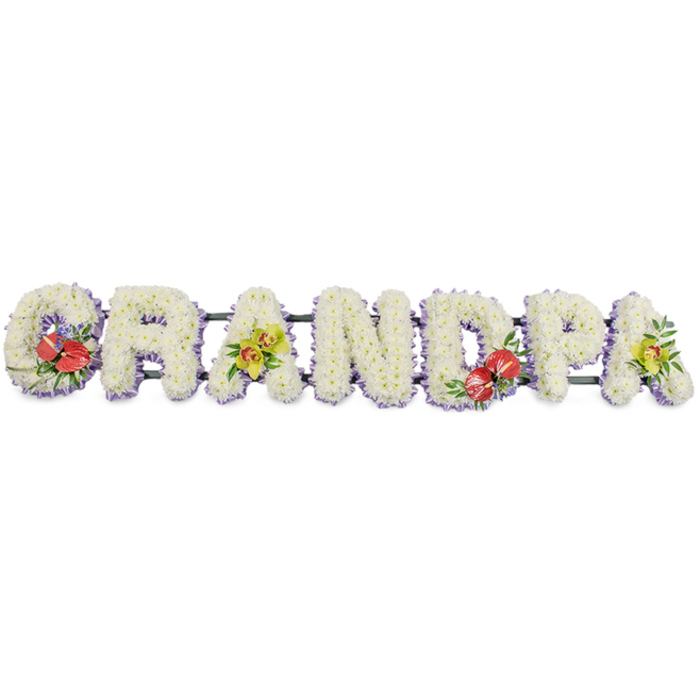This personalised funeral flower design spells out the word "GRANDPA" in a straight horizontal line, the boldness of the letters softened by an abundance of white blooms and gentle colour touches, as if prepared for a service in one of High Wycombe's churches. Each letter is formed from a solid bed of white chrysanthemums, their compact, round heads placed so closely that no gap is visible, creating a deep, cushion-like form. The myriad small petals catch the light, giving the arrangement a soft, velvety look that conveys peace, innocence, and a sense of eternal rest. Along the base of each letter, a slim border of pale lavender ribbon is just visible, adding a cool lilac outline that frames the flowers and subtly defines the shapes without overpowering them. The letters are aligned in a single word and supported from behind by dark green bars that keep the tribute straight and stable while remaining discreet. The careful monotone of white is gently broken by four thoughtfully placed floral sprays. On the far left, the 'G' carries shiny red anthuriums, their heart-shaped, waxy petals and upright yellow centres nestled into lush green foliage and hints of deeper tones, forming a bold expression of love and remembrance. The first 'A' is decorated with yellow-green orchids, their delicate petals and patterned throats emerging from bright leaves, offering a note of refined beauty. The 'D' in the centre-right repeats the red anthurium spray, providing visual balance, and the final 'A' echoes the first with another grouping of lime-coloured orchids and greenery. The result is a dignified, custom-made tribute, the kind of arrangement a family in High Wycombe might send for same-day delivery to a local crematorium or chapel, when they wish to mark a grandfather's life with quiet elegance and heartfelt respect.