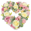The image shows a lush, heart-shaped floral tribute, crafted with pastel flowers and soft greenery, the kind of arrangement often chosen for funerals and memorials in High Wycombe and nearby villages. The heart is densely packed, almost pillow-like with petals, so that the flowers form a continuous, unbroken surface. Cream and light yellow roses are dotted throughout the design, their rounded, velvety blooms opening in smooth, gentle spirals that convey calm and dignity. Between these roses, clusters of light pink carnations create a delicate, textured fill, their frilled petals overlapping in layers that feel warm and comforting, like a gentle touch on the shoulder. Deeper tones come from mauve and magenta-pink lisianthus blooms, their slightly flared, bell-shaped flowers adding a note of thoughtful depth amid the softer shades. Silvery-green eucalyptus foliage frames the heart and weaves between the blossoms, its round leaves providing a cool, tranquil contrast and naturally guiding the eye around the shape. Tiny yellow-green buds appear here and there, offering small, hopeful accents within the pastel palette. The composition is harmonious and symmetrical, with carefully balanced colours and textures that suggest the steady hand of an experienced local florist. Against the clean white background, every detail stands out clearly, from the softness of the petals to the cool sheen of the eucalyptus leaves. This heart wreath would be fitting as a central tribute at a crematorium service in High Wycombe, beside a photo display at a wake, or delivered to a family home, expressing enduring love, cherished memories, and gentle sympathy in a visual language that needs no words.